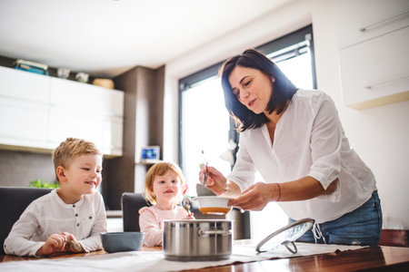 Grandma takes care of the grandchildren while their parents are at work, serving lunch to kids, putting soup in plate.の写真素材