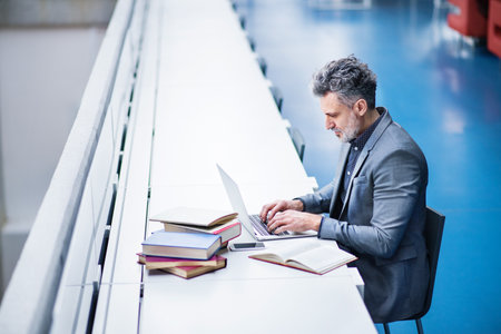 Handsome businessman working on laptop, searching for informations in book. Traditional information source in modern office space.の写真素材