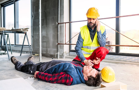 Colleague giving first aid to unconscious worker after accident, calling ambulance. Concept of occupational safety and health in workplace.の写真素材