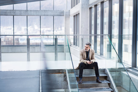 Handsome businessman sitting on stairs in modern office hallway.の写真素材