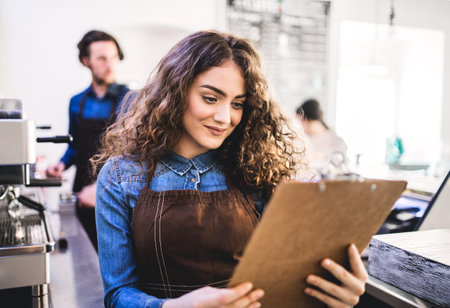 Two young baristas working in coffee shop, standing by counter. University students working part-time in cafe.の写真素材