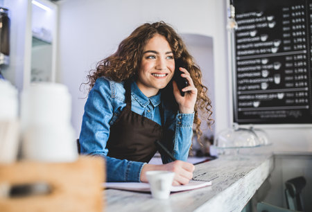Beautiful female barista working in coffee shop, phone order. University student working part-time in cafe.の写真素材