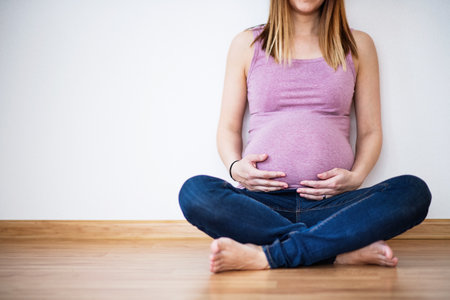 Pregnant woman sitting on floor touching her belly.の写真素材