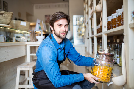 Handsome man working in package-free store using reusable containers. Zero waste shops offering package-free bulk goods and sustainable alternatives.の写真素材
