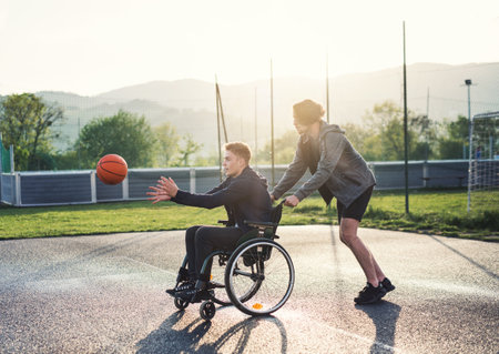 Disabled young man in a wheelchair playing basketball with his friends. Teamwrok and male friendship.の写真素材