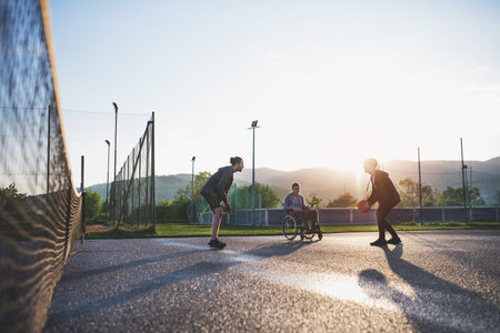 Disabled young man in a wheelchair playing basketball with his friends. Teamwrok and male friendship.の写真素材