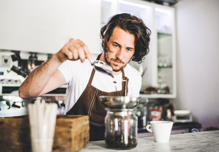 Handsome barista working in coffee shop, preparing coffee. University student working part-time in...