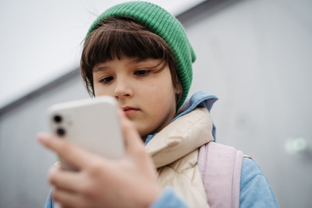 Girl standing outdoors, scrolling on smartphone. Using social media. Online bullying or cyberbullying for young schoolgirl.の写真素材