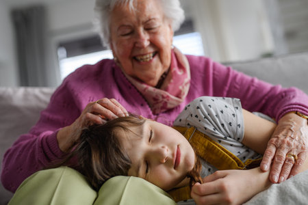 Sleeping girl lying head on gradmother knees. Portrait of an elderly woman spending time with granddaughter.の写真素材