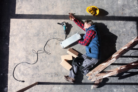 Male worker lying on the floor after fall from ladder, holding his knee. Work injury, accident in workplace.の写真素材
