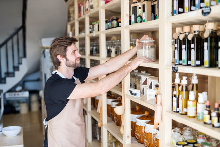 Handsome man working in package-free store using reusable containers. Zero waste shops offering...