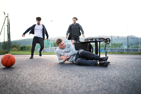 Young disabled man fall off wheelchair, fiends helping to sit back. Male friendship.の写真素材