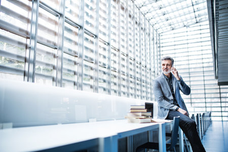 Handsome businessman phone calling, searching for informations in books. Traditional information...