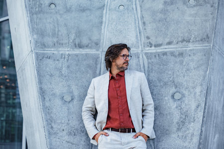 Portrait of mature businessman standing on city street, in front of office building. Handsome man...