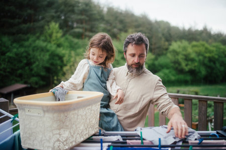 Girl helping father with household chores, hanging clothes on drying rack. Fatherhood and Fathers...