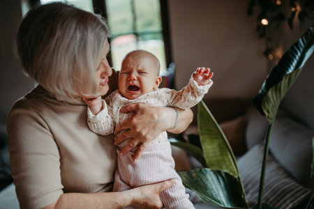 Grandmother holding crying baby girl in arms, calming her down, soothing her. Strong bond between grandparent and grandchild.の写真素材