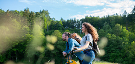 Travellers couple going on e-bike ride in nature. Tourist riding electric bicycles on easy trail road in the middle of forest. Young tourist spending summer vacation oudoors.の写真素材