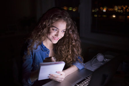 A beautiful university student having evening online class, e-learning sitting at home. Online consultation.の写真素材