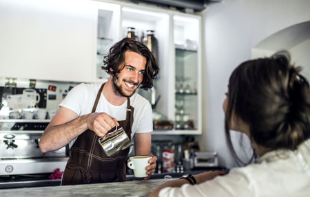 Handsome barista working in coffee shop, preparing coffee. University student working part-time in...