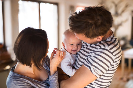 Happy parents holding and playing with small baby, carrying him around house. Unconditional paternal love, family moment.の写真素材