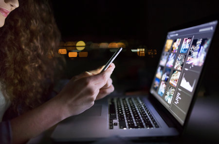 Close up of university student is writing her thesis on a laptop at night, sitting at home at table,...