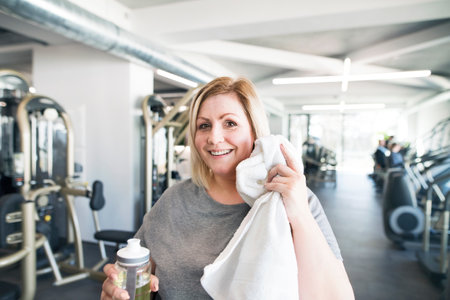 Overweight woman resting after workout in gym. Wipe sweat from face with towel.の写真素材