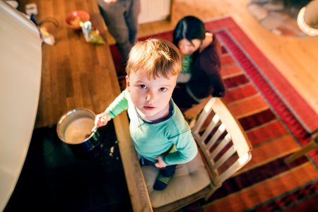 Happy parents holding with kids in kitchen. Older brother stirring porridge in pot. Unconditional...