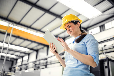 Female project manager standing in modern industrial factory. Manufacturing facility with robotics,...