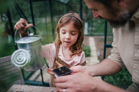Fater and girl working together in garden, watering seedlings, spending time togeter, have shared hobby. Fatherhood and Fathers Day concept.の写真素材