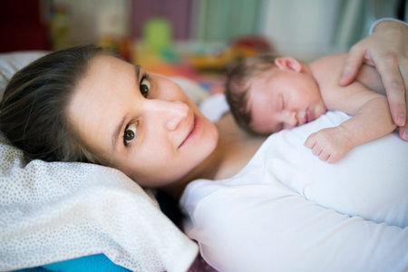 New mom lying on bed by newborn baby girl. Unconditional paternal love, idyllic family moment.