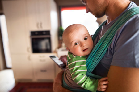 Father holding small baby, carrying him around house in baby carrier. Unconditional paternal love,...