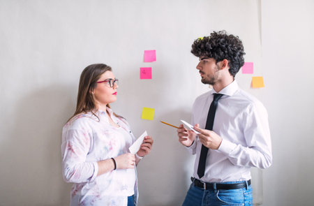 Two colleagues talking, working on a new project together in a startup company office. Working in...