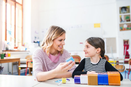 Hardworking teacher learning with young schoolgirl in classroom, explaining her shapes and math, geometry.の写真素材