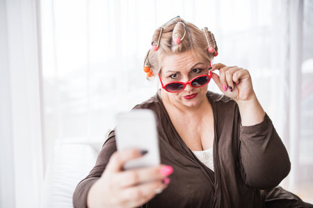 Portrait of beautiful young overweight looking at mirror, having fun. taking selfie with smartphone.