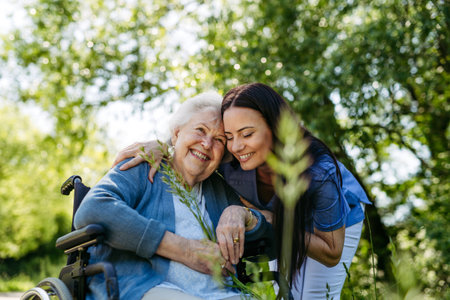 Female caregiver pushing senior woman in wheelchair. Nurse and elderly woman enjoying a warm day in...