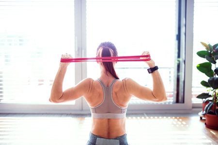 Beautiful redhead womans home fitness routine with resistance band. Home workout on gym mat in...