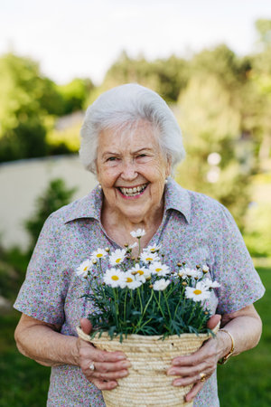 Portrait of beautiful older woman holding basket pot with daises, smiling.の写真素材