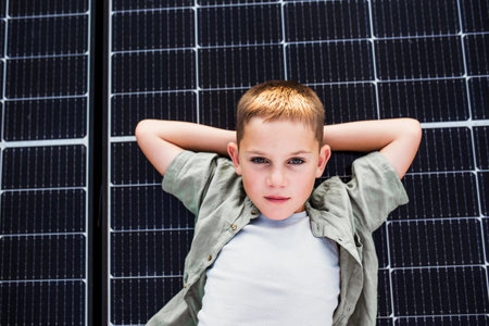 Top view of boy lying on roof with solar panels, looking at camera. Rooftop solar or photovoltaic...