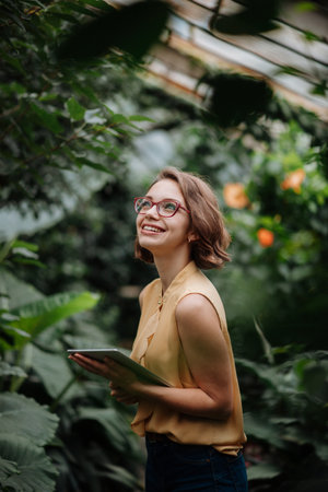 Businesswoman with tablet, standing in botanical garden, in the middle of lush green foliage,...