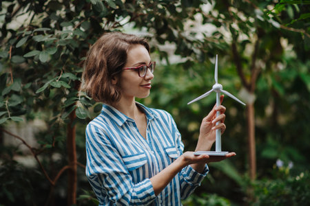 Beautiful woman standing in botanical garden, in the middle of lush green foliage, holding model of...