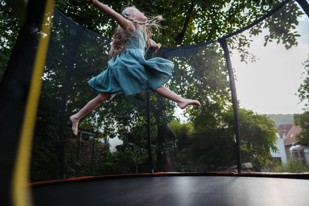 Little girl jumping on trampoline in the backyard. Dangers and risks of trampoline for kids.