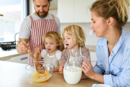 Young nuclear family making pancakes together. Parents and children in kitchen, preparing pancake...