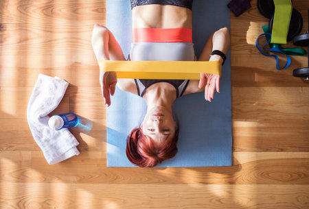 Top view of redhead womans home fitness routine with resistance band. Home workout on gym mat in living room, sporty woman wearing sportswear.の写真素材