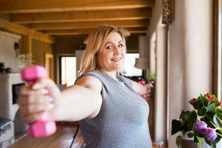 Overweight woman exercising at home, using dumbbells. Workout in living room.