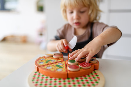 Boy playing with wooden toys in living room, serving and cutting pizza.の写真素材