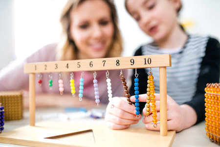 Hardworking teacher learning with young schoolgirl in classroom, explaining math problem, using education tools.の写真素材