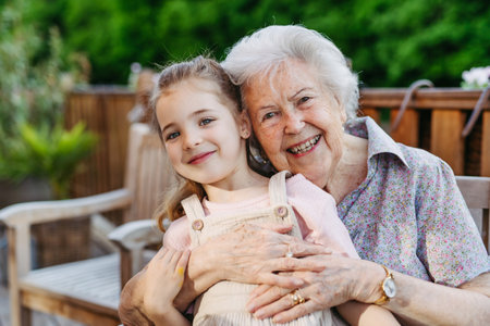 Portrait of granddaughter and elderly grandma on patio. Senior lady spending time with young girl, enjoying together time.の写真素材