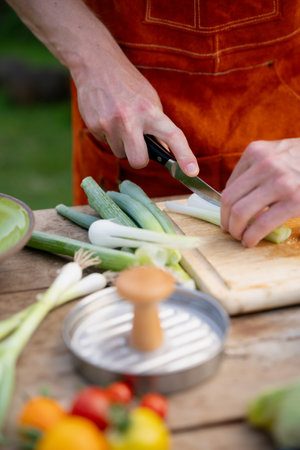 Close up of man holding sharp knife, cutting spring onion. Preparing vegetables for an outdoor barbecue.の写真素材
