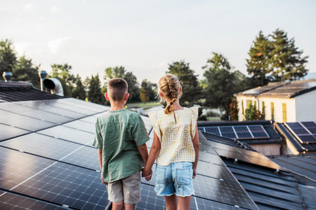 Two young siblings on roof with solar panels, holding each other. Rooftop solar or photovoltaic system. Sustainable future for next generation.の写真素材