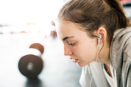 Young fitness girl with sweat on face feeling exhausted after hard workout in gym, sitting and...
